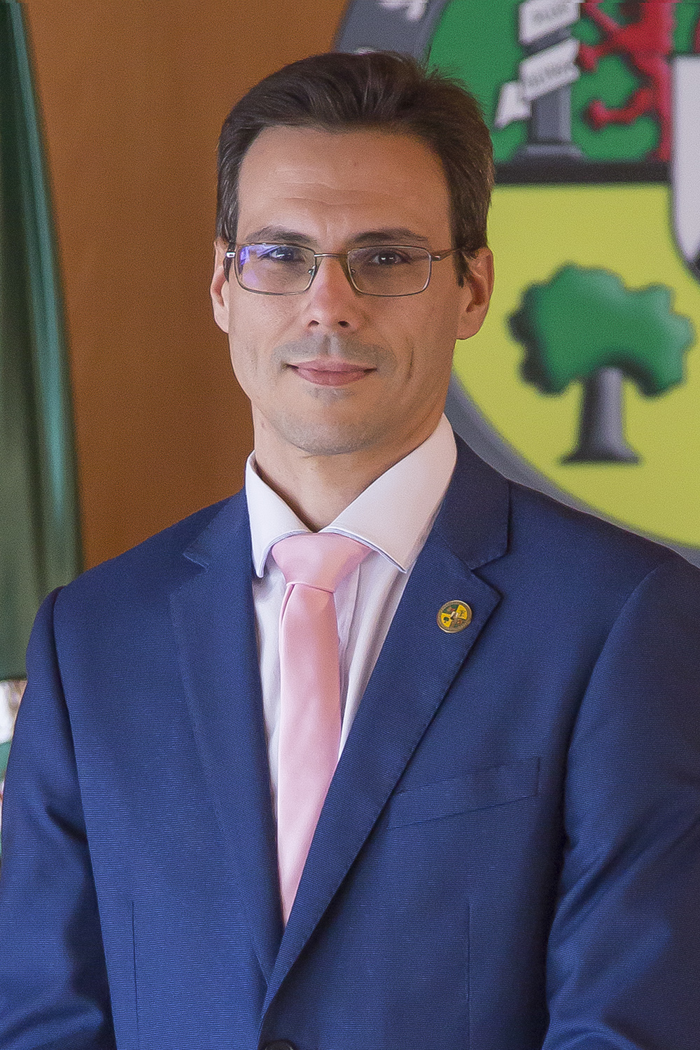 Foto oficial tipo retrato de Javier Berrocal Olmeda delante de una pared con la bandera y el logo de la universidad.