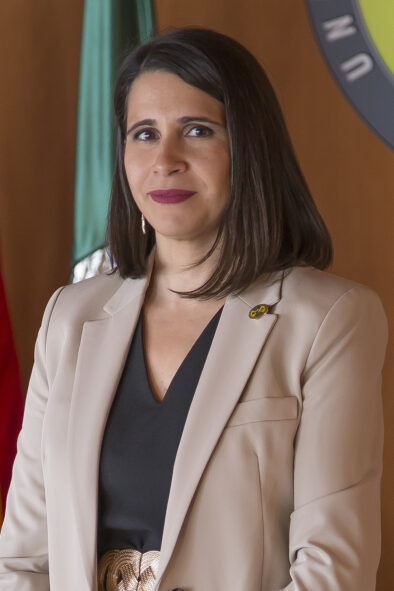 Foto oficial tipo retrato de Rocío Blas Morato delante de una pared con la bandera y el logo de la universidad.
