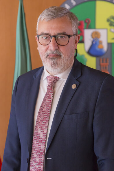 Foto oficial tipo retrato de Francisco Álvarez Arroyo delante de una pared con la bandera y el logo de la universidad.