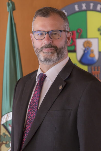 Foto oficial tipo retrato de Juan Francisco Panduro López delante de una pared con la bandera y el logo de la universidad.